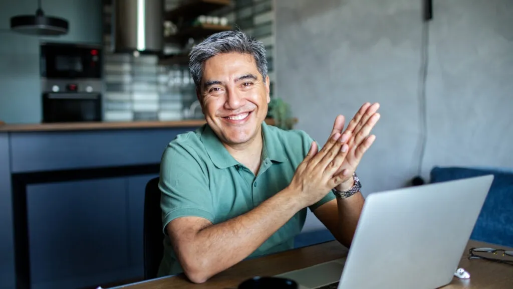 man in green shirt sitting by computer looking straight at camera