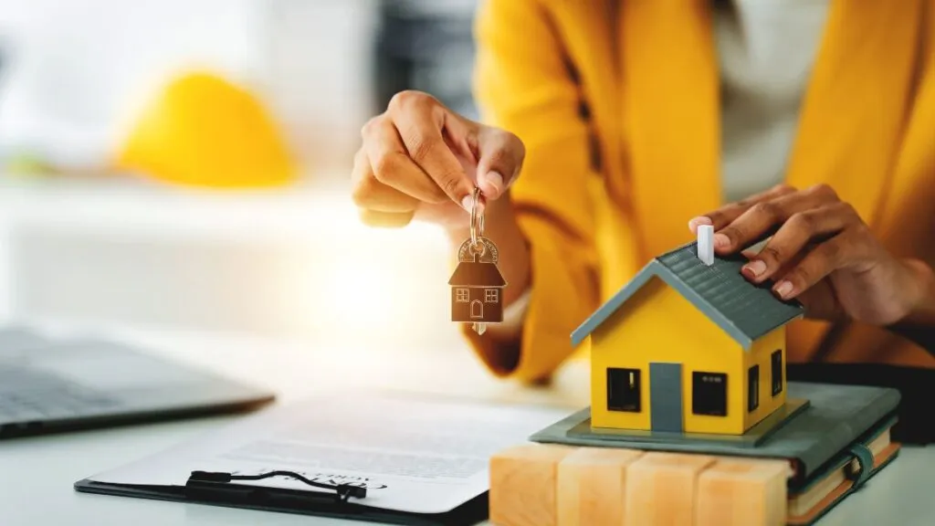 woman's hand holding a set of house keys next to a small house model
